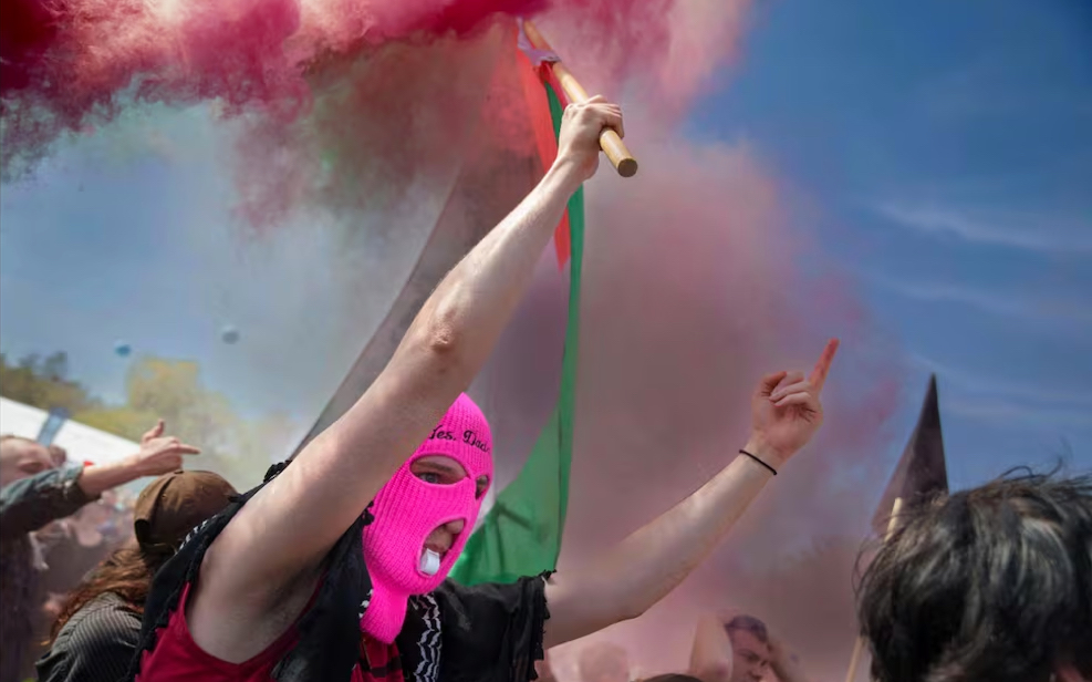 Un manifestante con una máscara sostiene una bandera palestina mientras la gente protesta durante el discurso del ministro de Justicia danés, Peter Hummelgaard, con motivo del Día Internacional de los Trabajadores en Faelledparken en Copenhague, Dinamarca, el 1 de mayo de 2025. Foto: EFE