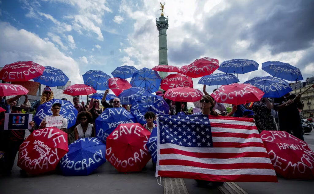 Varias personas sostienen paraguas con la leyenda “salvemos la democracia” participan en la movilización mundial llamada "Sin reyes", en París, contra las políticas antimigrantes de Trump, el sábado 14 de junio de 2025. Foto: AP