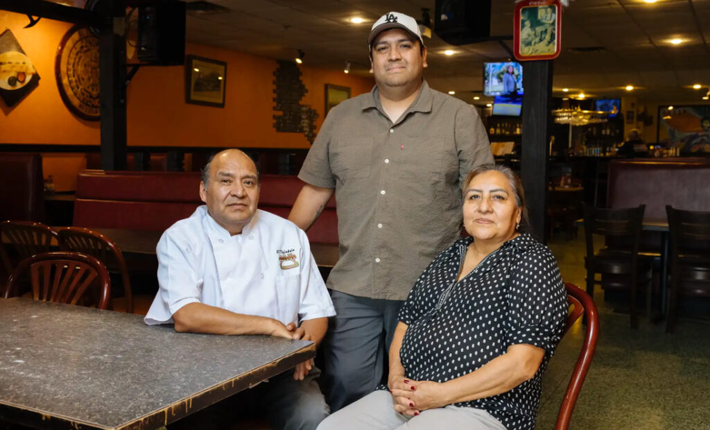 Miguel Hernández Jr. (centro) con su padre, Miguel Hernández Sr. (izquierda) y su madre, Rosa Zambrano, en El Tejaban Mexican Grill en Richfield. Hernández Sr. y Zambrano emigraron a Estados Unidos desde México y abrieron su primer restaurante en 2008. Hernández Jr. ahora dirige una burritería temporal dentro del restaurante de sus padres. Carly Danek para MPR News